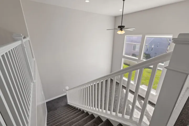 High ceilings with recessed lighting, modern ceiling fan, multiple large windows, and white balustrade staircase with carpeted treads