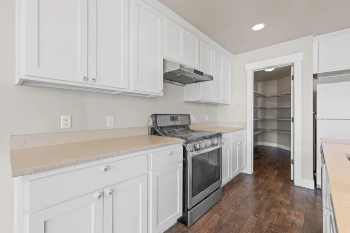 White shaker cabinetry, light-toned countertops, wood-finish flooring, stainless steel range, and a walk-in pantry