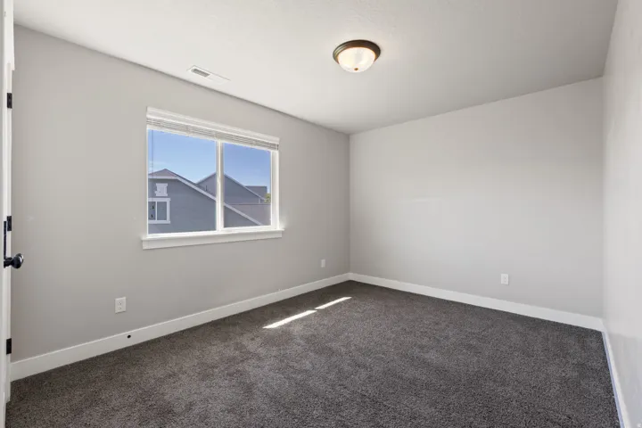 Neutral paint palette, dark carpet flooring, window with blinds, flush mount ceiling light, and a black door handle