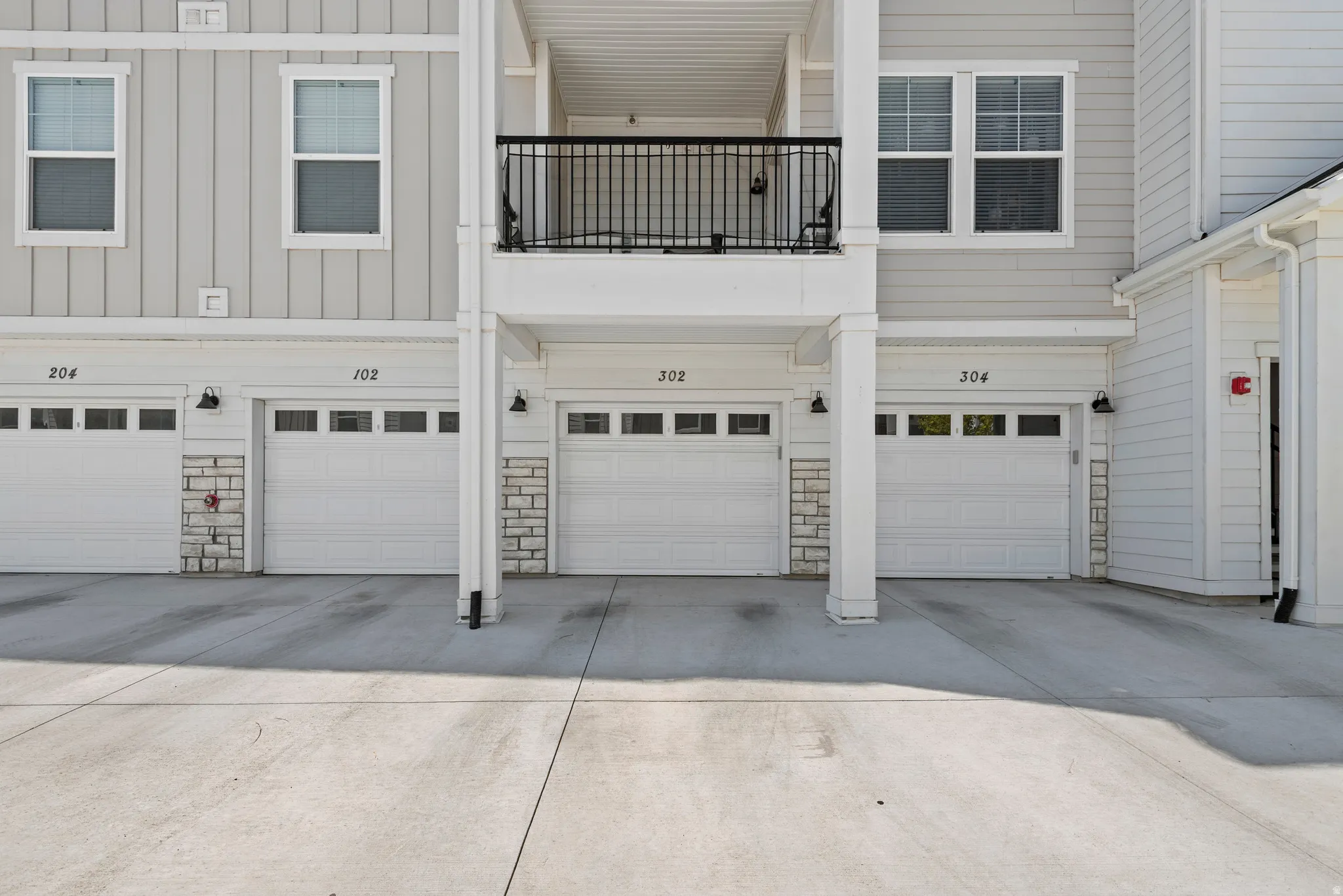 Exterior featuring vertical siding, individual garage doors with transom windows, stone veneer accents, and a second-story balcony with black railings