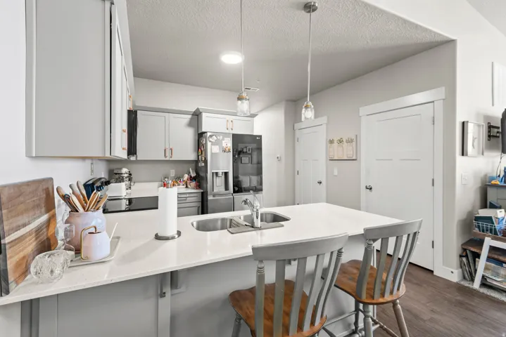 Kitchen featuring light gray cabinetry, stainless steel appliances, a center island with sink, and pendant lighting