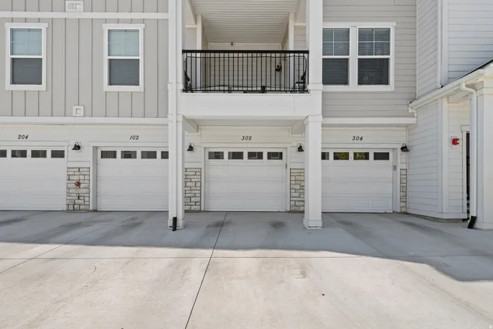 Exterior featuring vertical siding, individual garage doors with transom windows, stone veneer accents, and a second-story balcony with black railings
