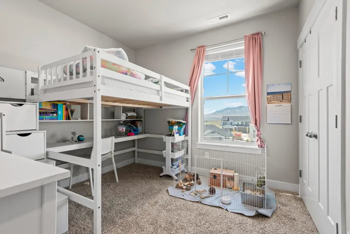 Carpeted room featuring a white interior door, a large window, and a built-in loft bed with integrated shelving and desk space