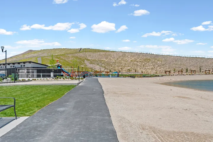 Manicured lawn, paved walkway, sandy beach, body of water, and distant hills