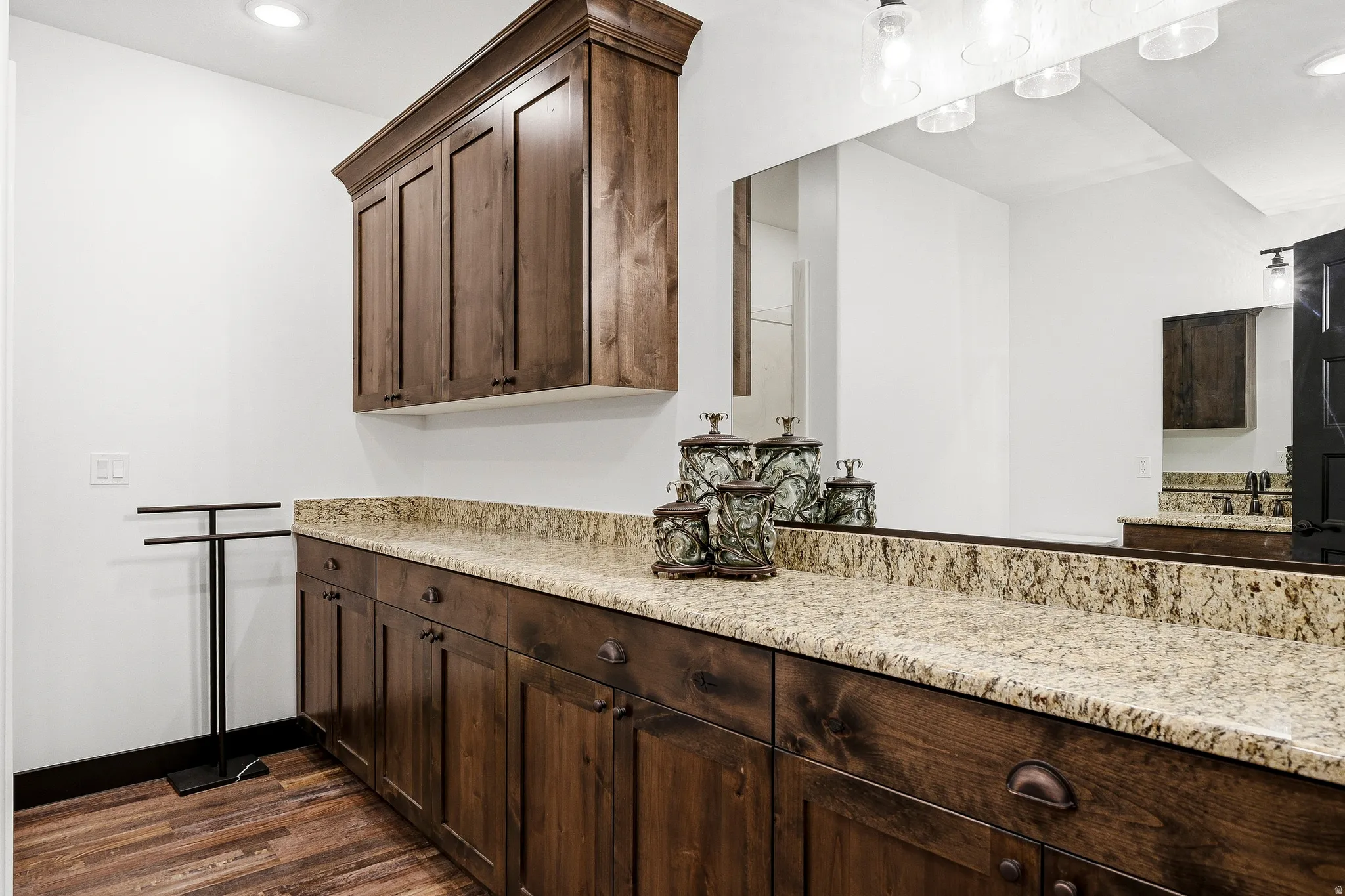 Wood-finish flooring, custom wood cabinetry, extensive countertop space, integrated vanity lighting, and full-wall mirror