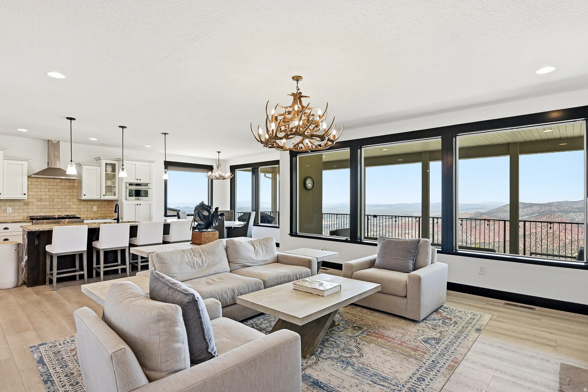 Open-concept living space featuring wood-finish flooring, a kitchen island with seating, white cabinetry, and extensive windows with dark trim