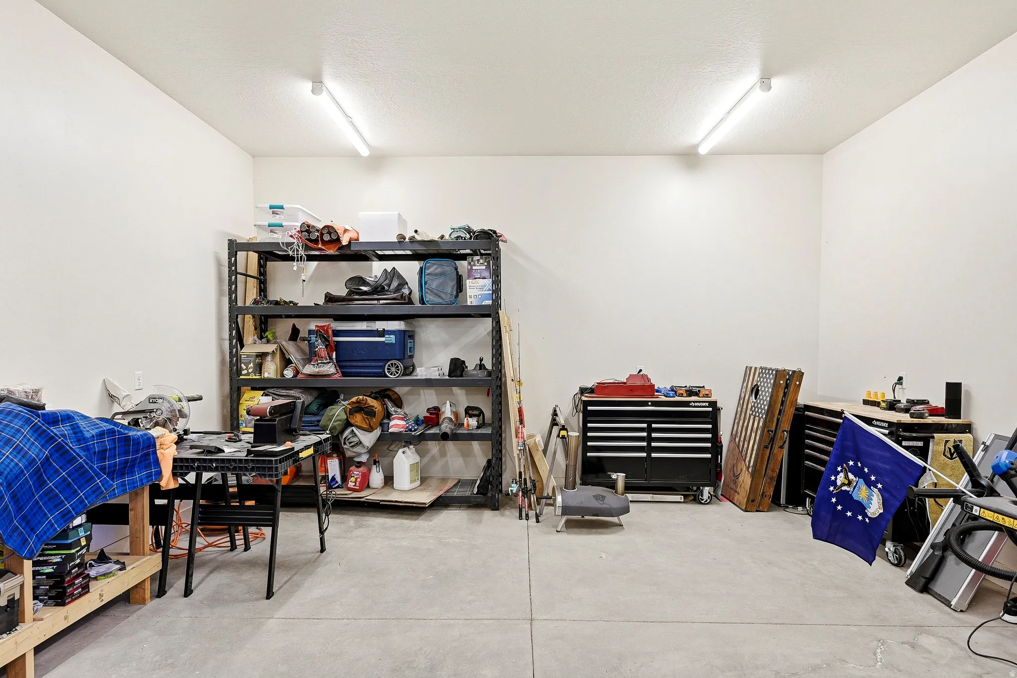 Concrete flooring with ample open space, overhead fluorescent lighting, and white painted walls