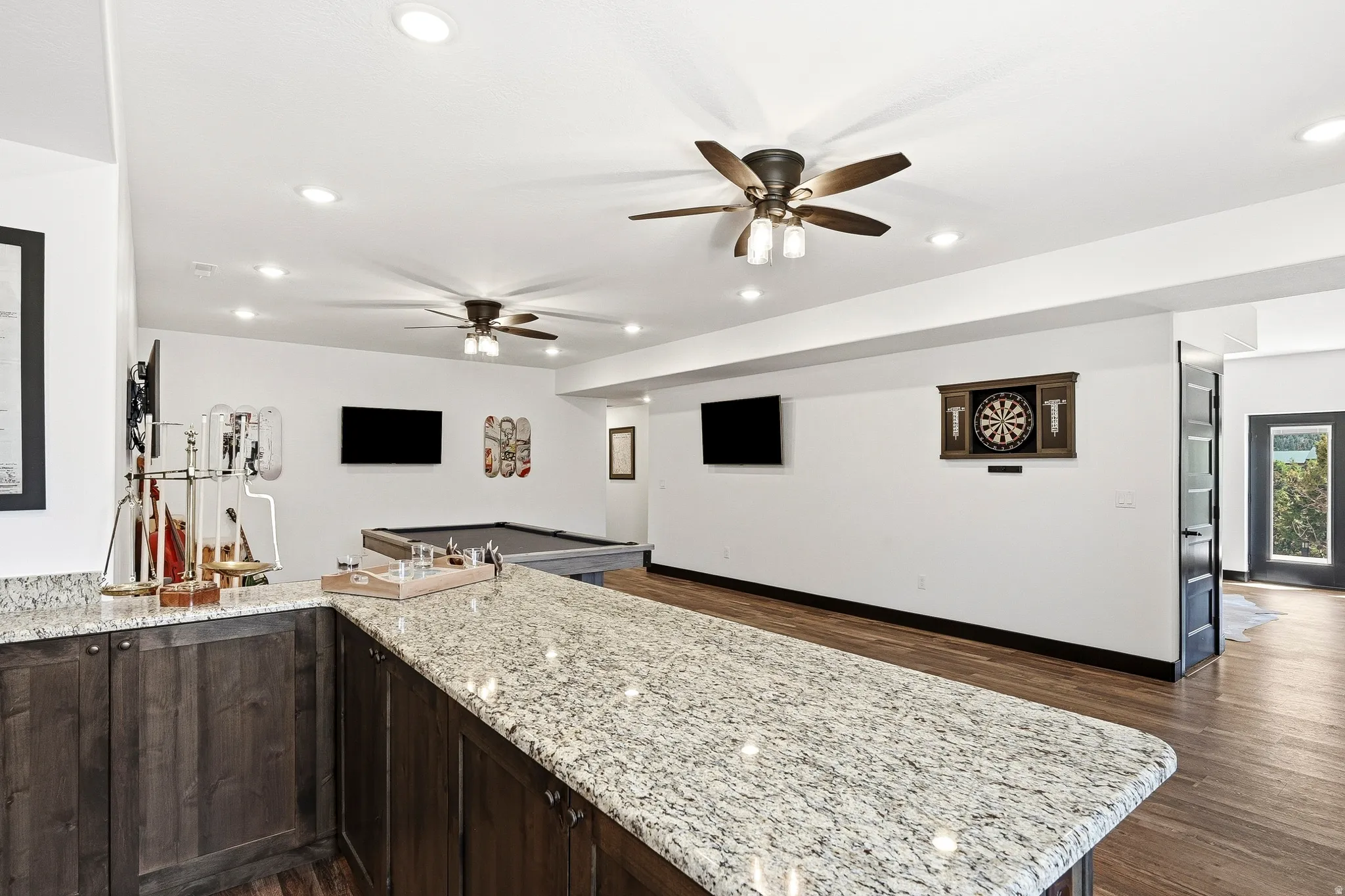 Granite countertop bar with wood-finish cabinetry, recessed lighting, ceiling fans, and wood-finish flooring