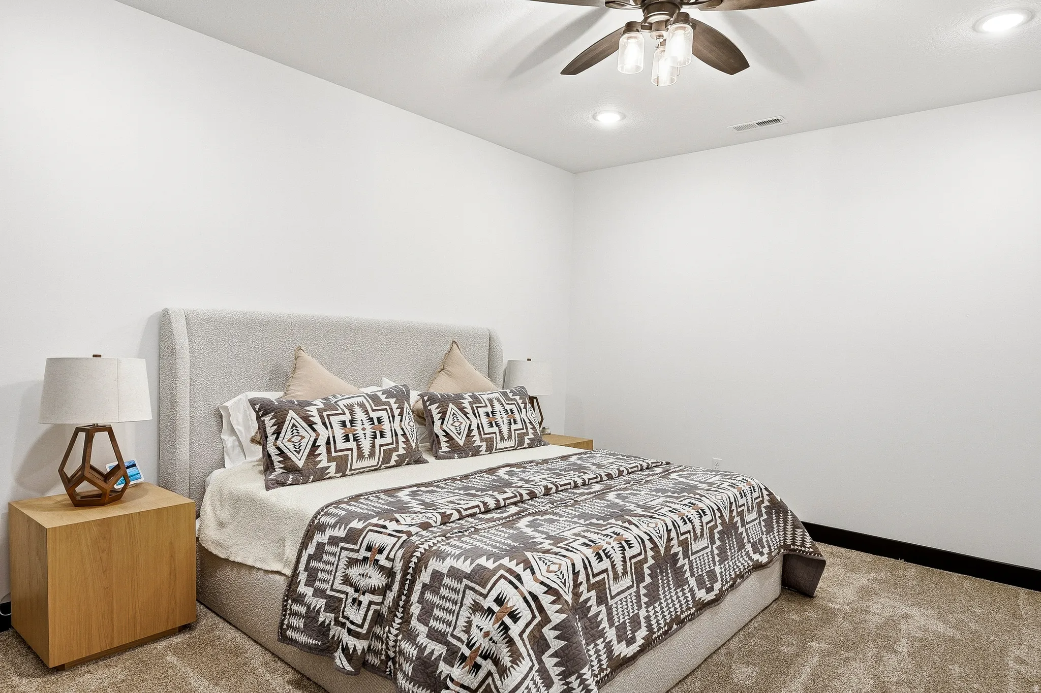 Recessed lighting, ceiling fan with light kit, textured carpet flooring, and a textured upholstered headboard