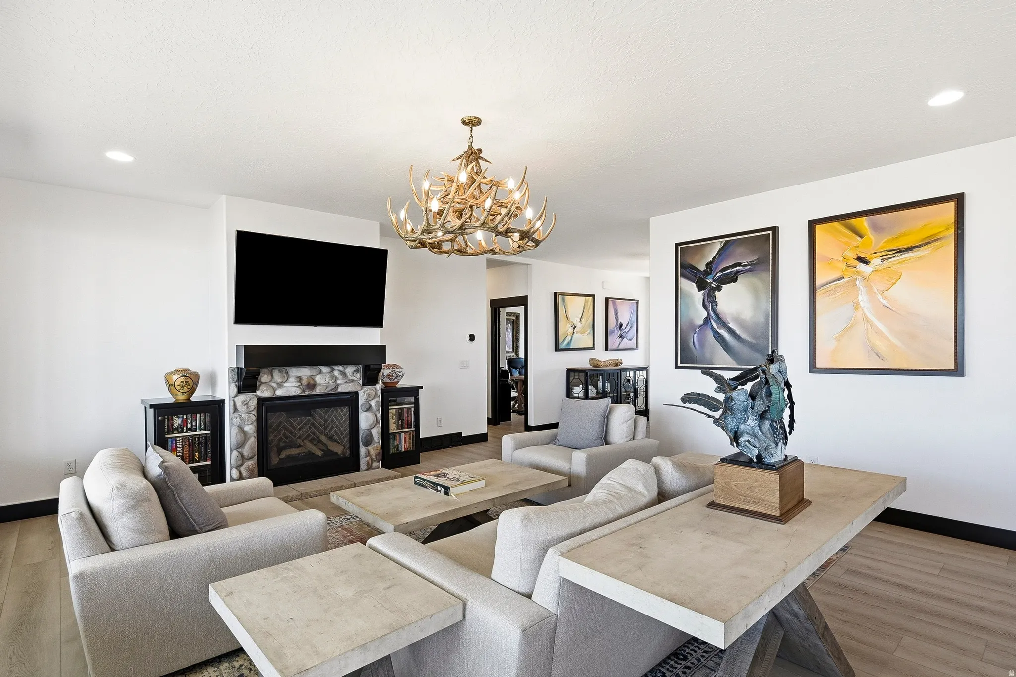 Living area featuring light wood-finish flooring, a stone-faced fireplace with a black mantel, and a multi-branch chandelier