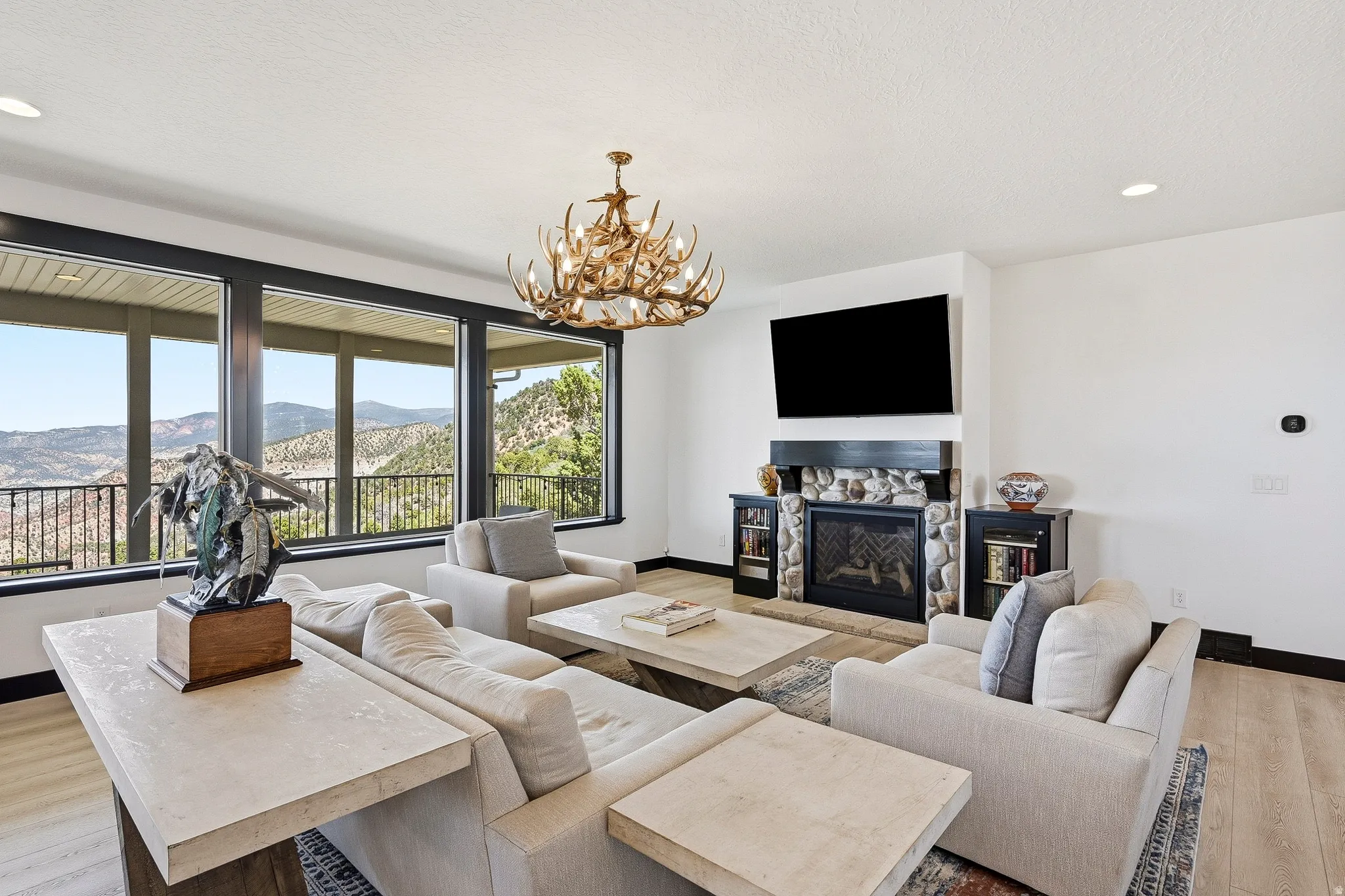 Spacious living area featuring large picture windows, wood-finish flooring, a stone-surround fireplace, and a decorative chandelier