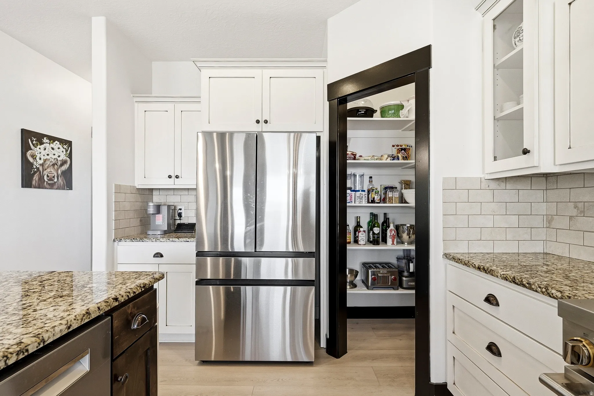 White cabinetry with dark hardware, stainless steel refrigerator, light-toned subway tile backsplash, and a walk-in pantry with shelving