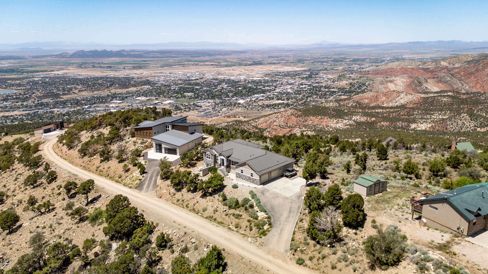 Elevated property with a large driveway, surrounded by natural desert landscaping and scattered trees