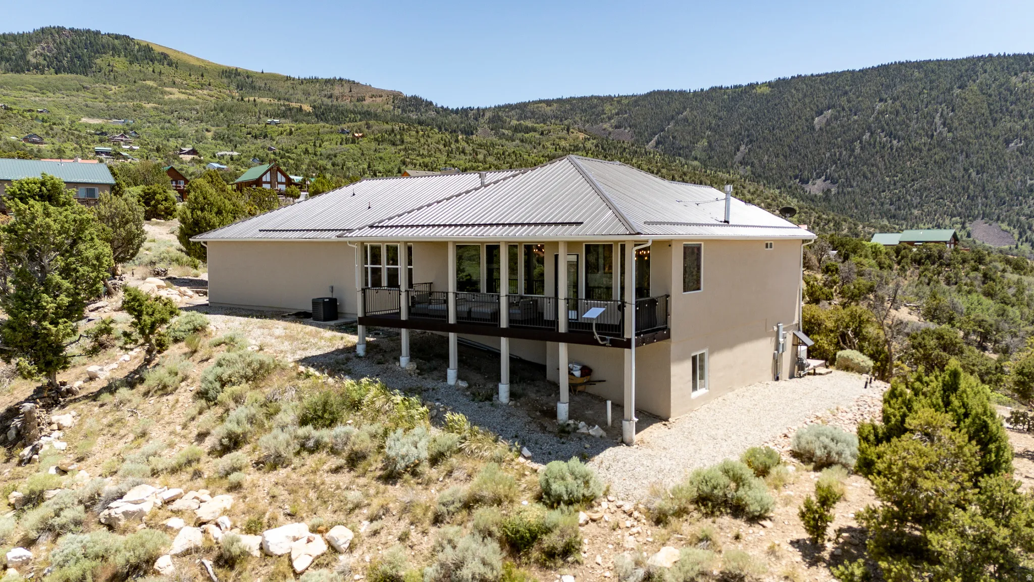 Stucco exterior with a corrugated metal roof, elevated rear deck with black railing, and numerous large windows