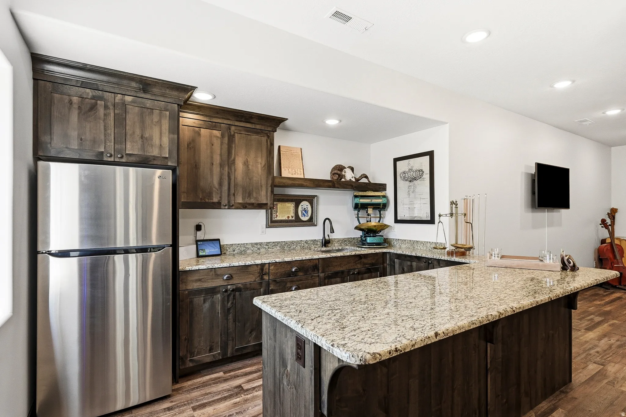 U-shaped kitchen island with granite countertops, wood-finish cabinetry, stainless steel refrigerator, and recessed lighting