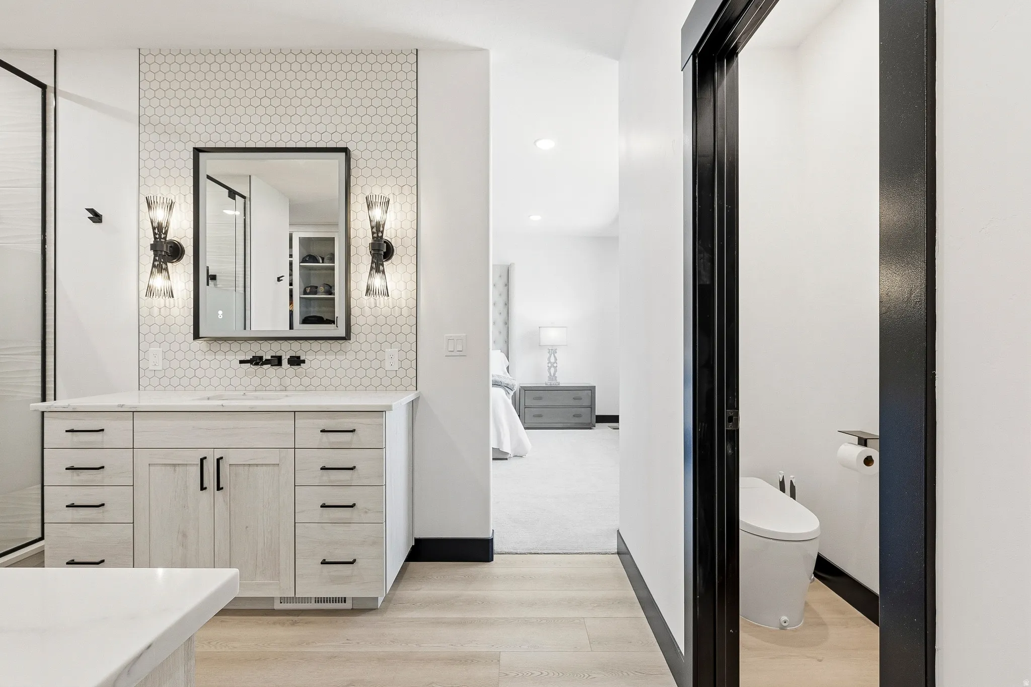 Vanity with light wood-finish cabinetry, white countertop, and hexagonal tile backsplash