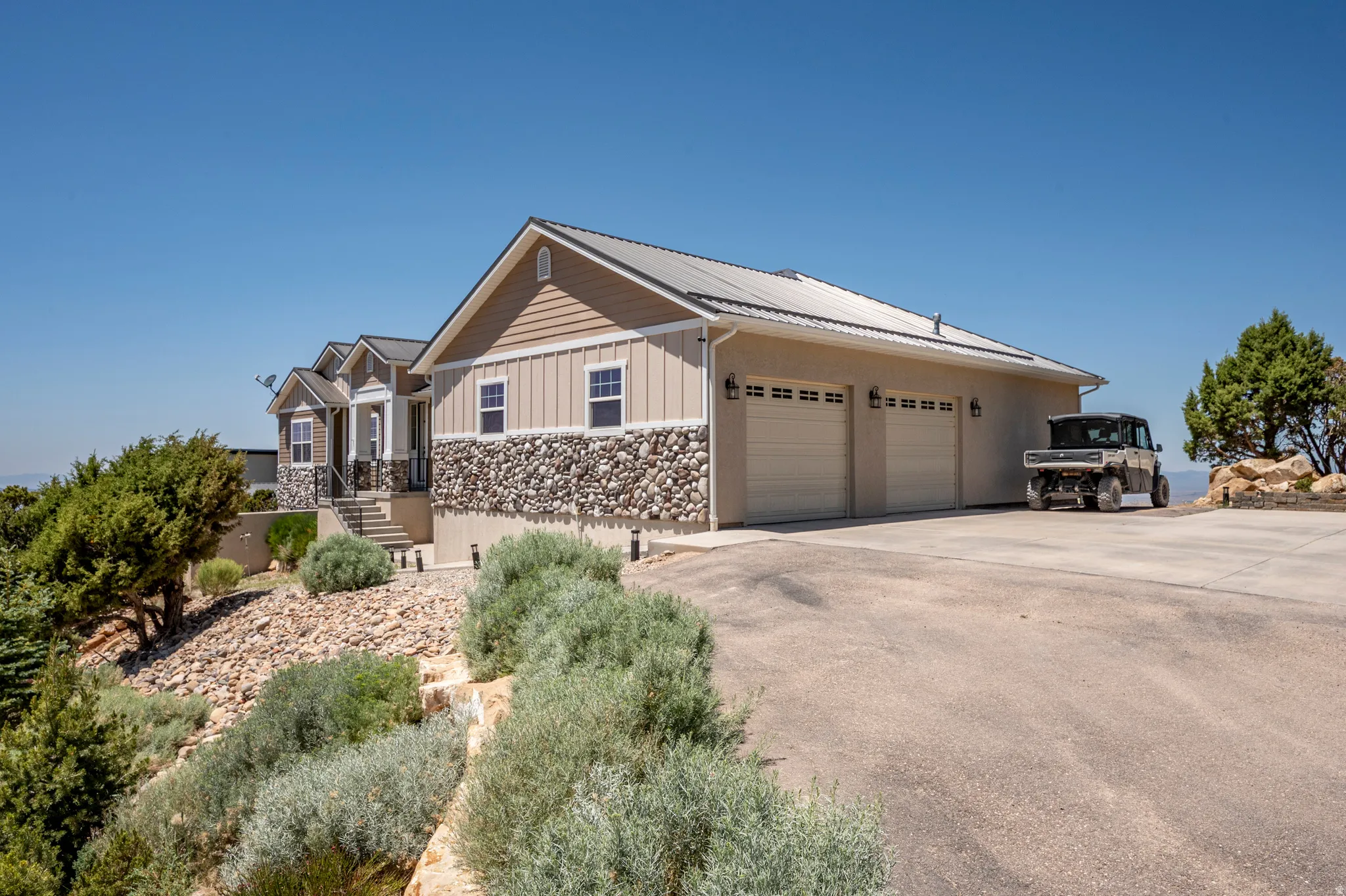 Exterior featuring stone and siding finishes, a metal roof, a three-car garage, and a tiered landscaped approach