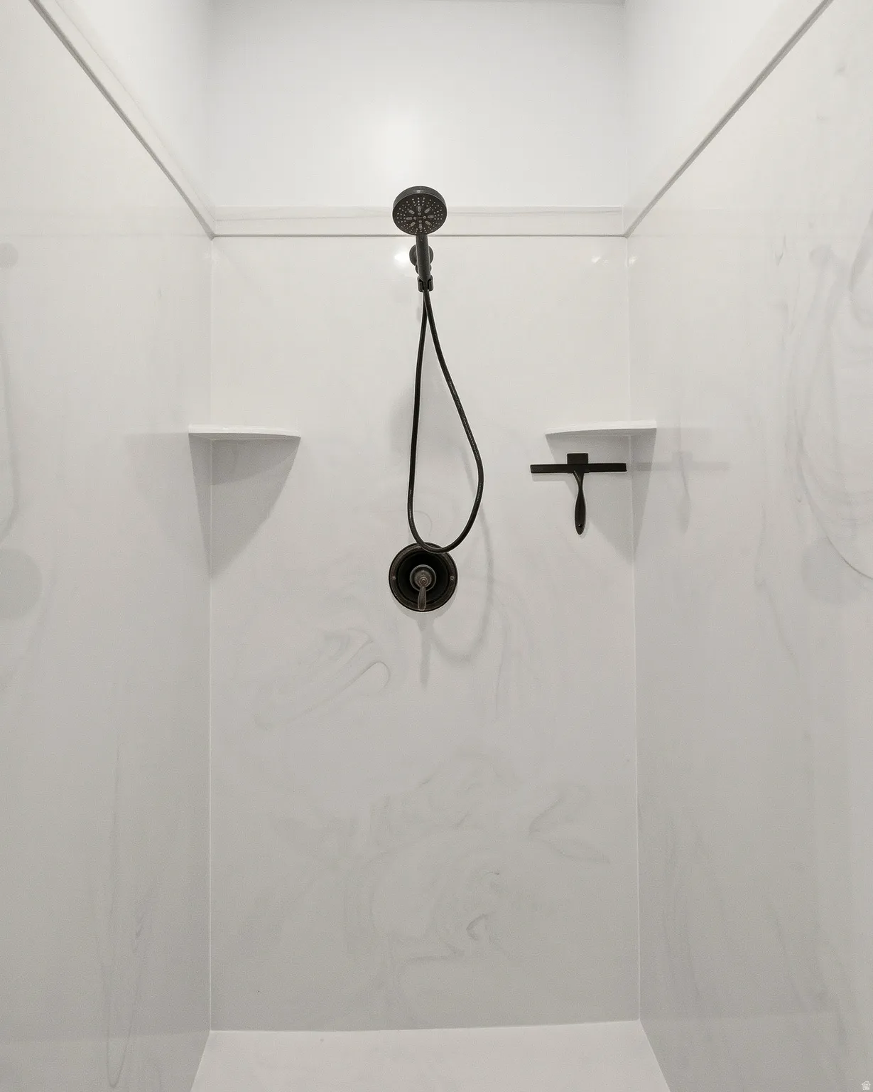 Shower enclosure with white swirled panels, dark bronze shower head and controls, and integrated corner shelves