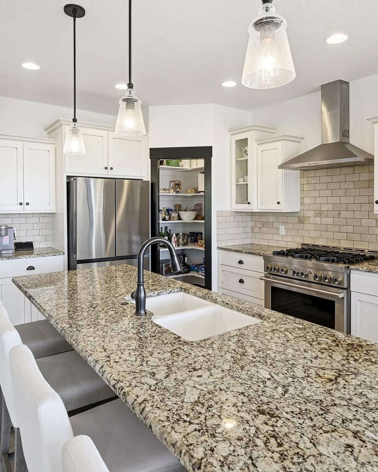 Kitchen featuring a large island with a double basin sink, stainless steel appliances, white cabinetry, a tiled backsplash, and recessed lighting