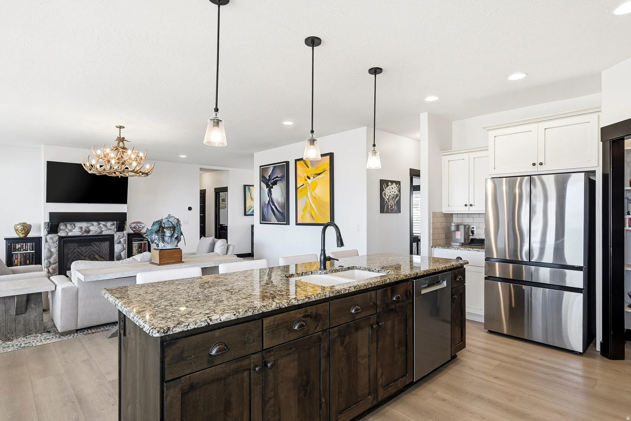 Kitchen island with granite countertop and integrated sink, stainless steel dishwasher, stainless steel French-door refrigerator, white upper cabinetry, and recessed lighting