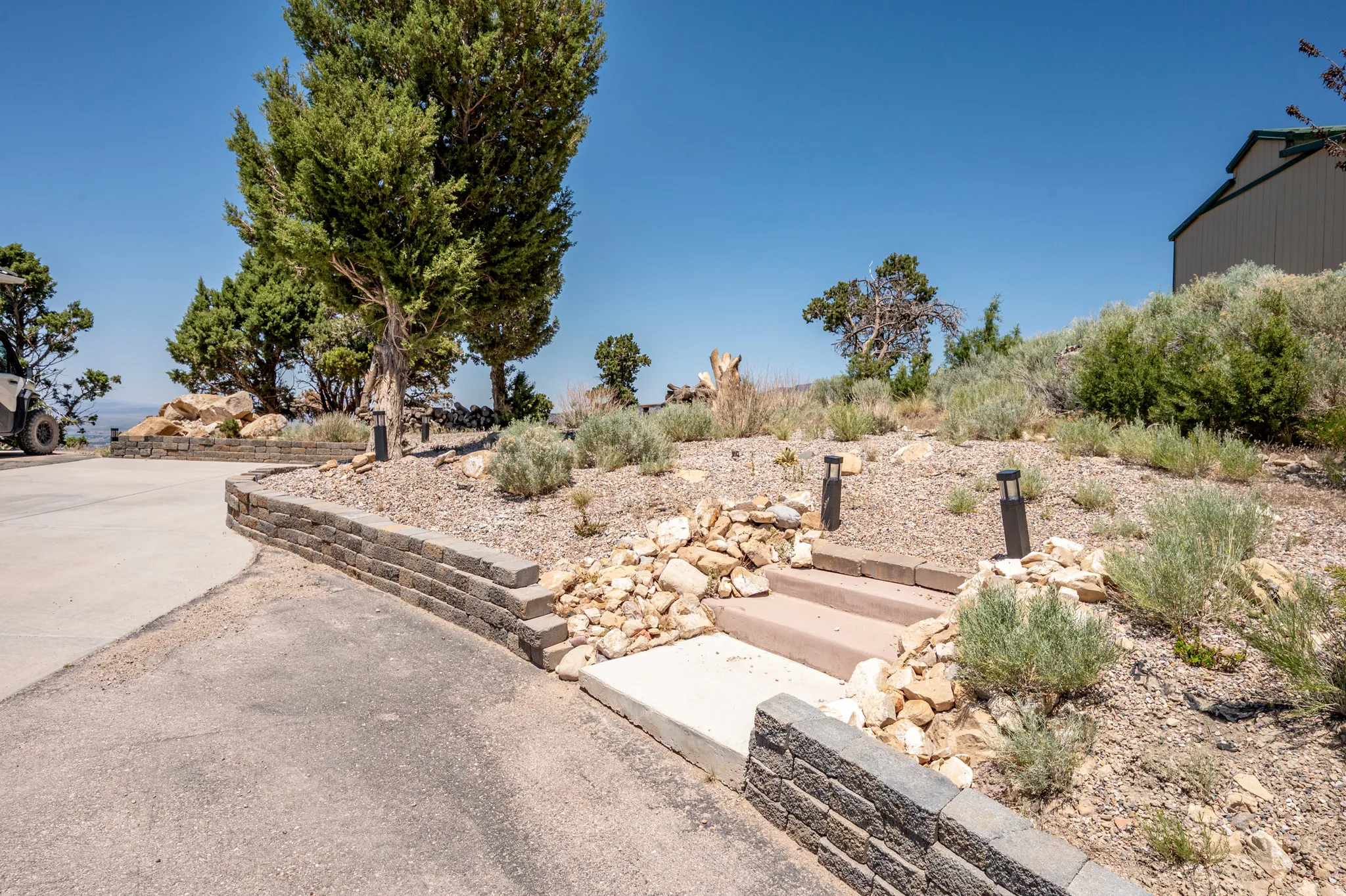 Segmented retaining wall, paved driveway, concrete steps, and landscaped hillside