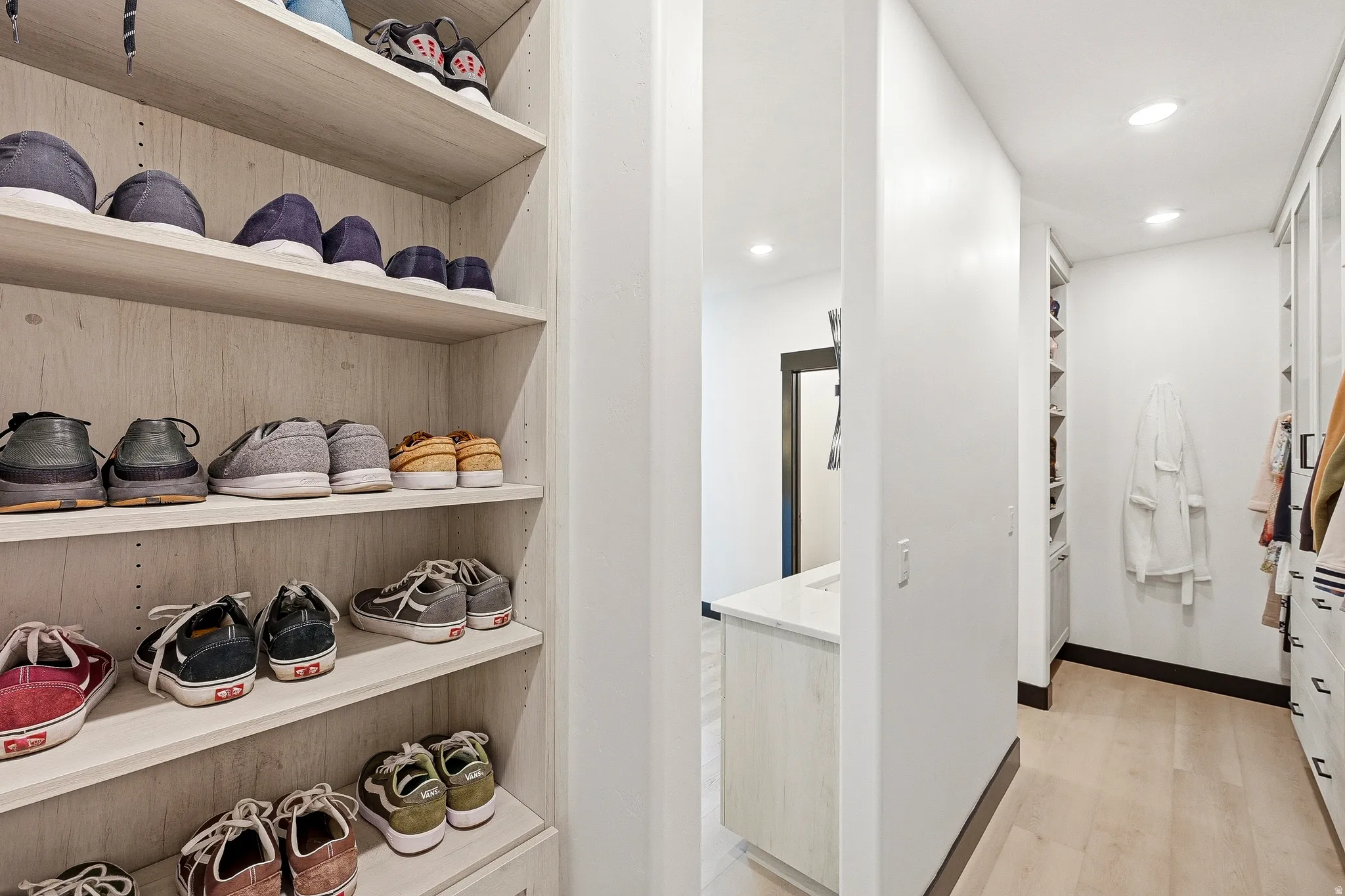 Custom built-in shelving, wood-finish flooring, recessed lighting, and a built-in vanity with a stone countertop