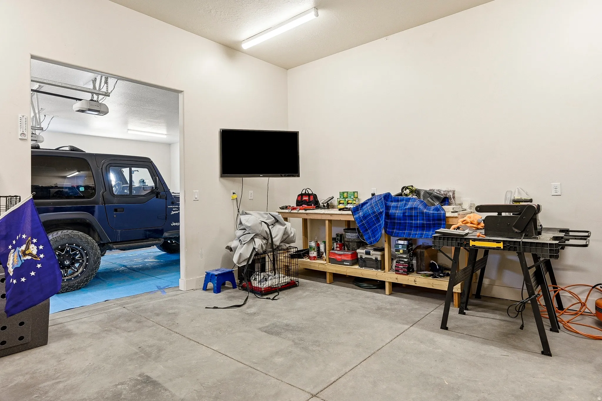Concrete flooring with a built-in workbench, overhead fluorescent lighting, and white painted walls
