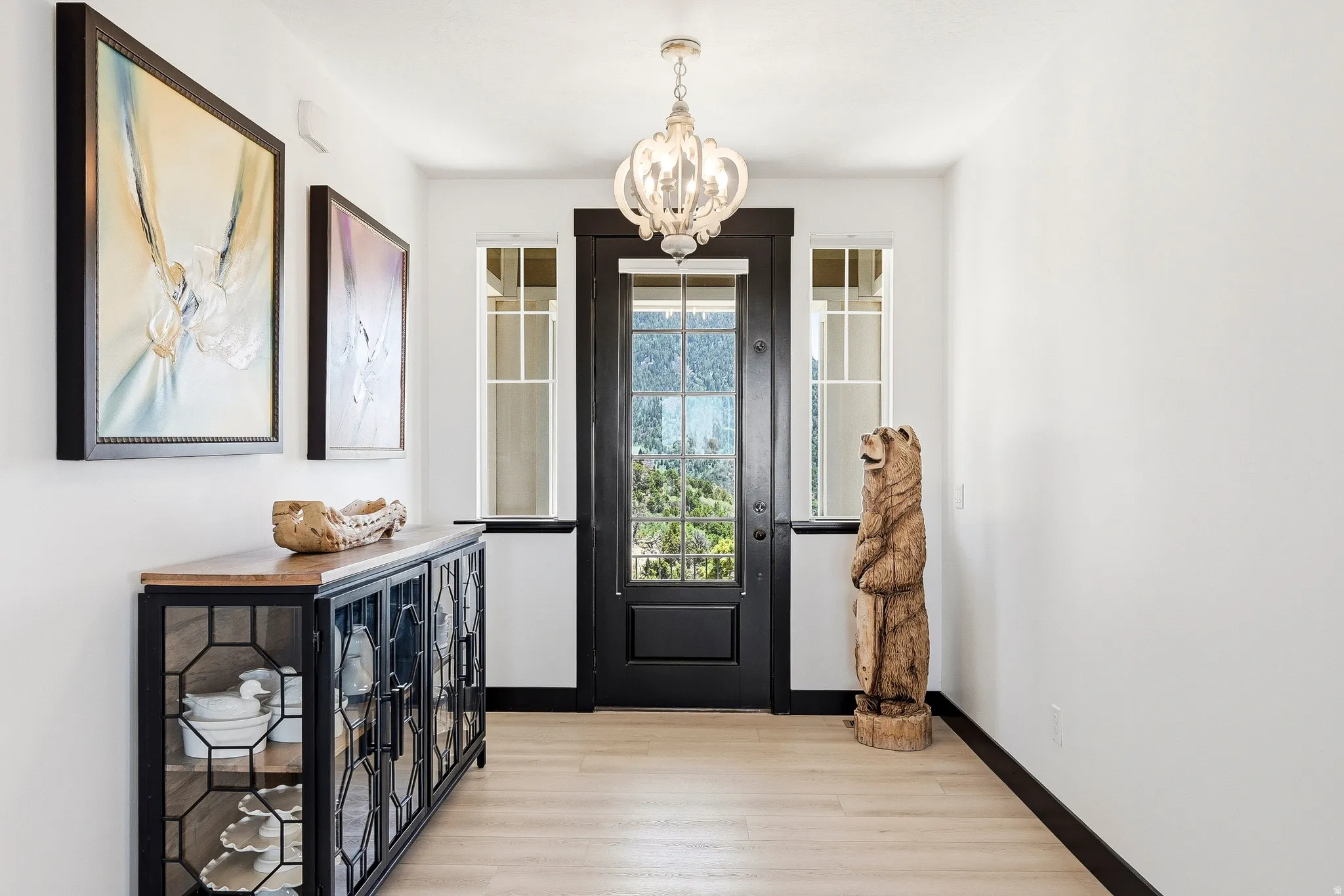 Entryway featuring a dark-paneled door with frosted glass, side windows with grid patterns, a decorative chandelier, and wood-finish flooring