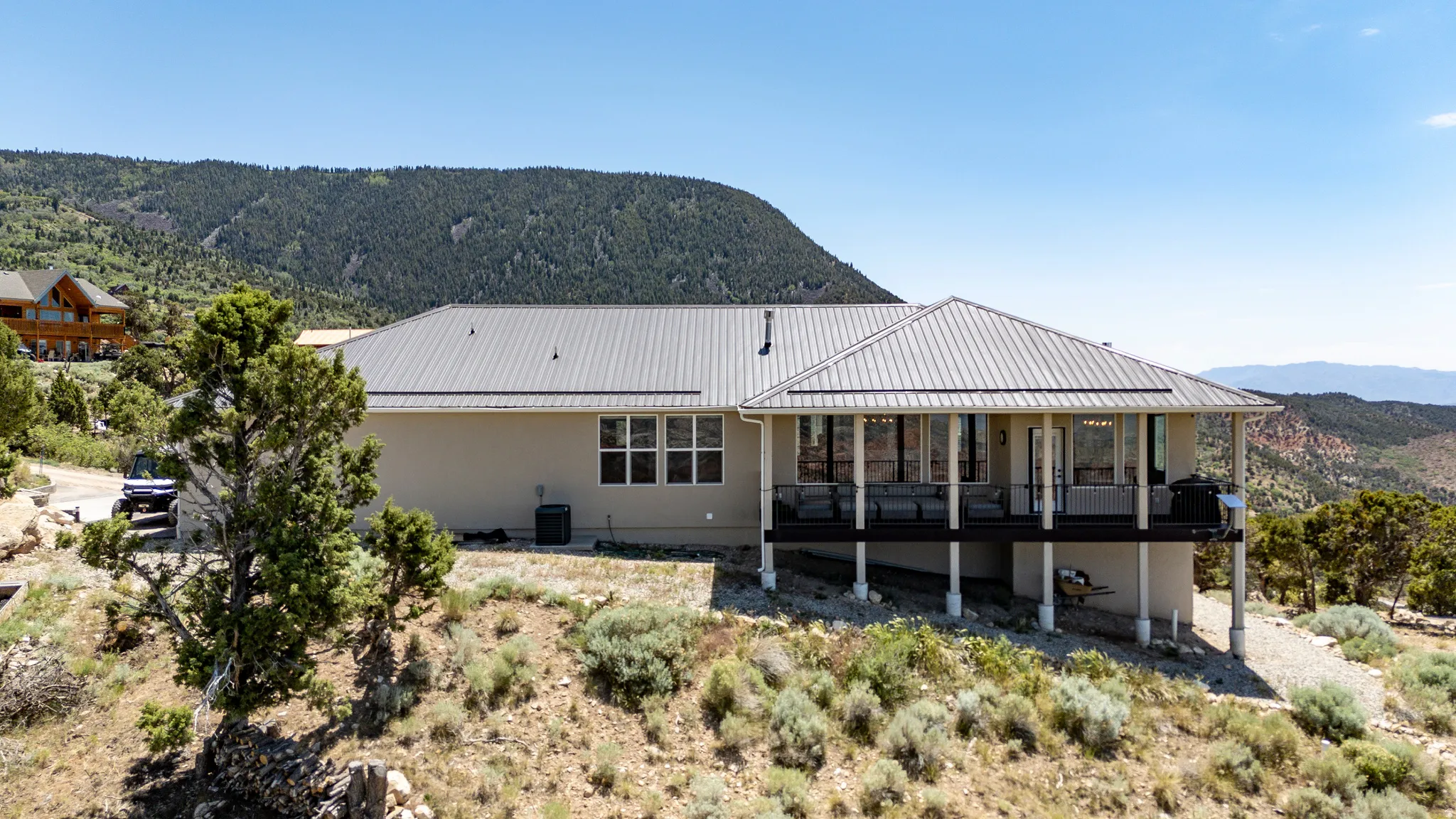Expansive rear deck, metal roofing, multiple windows, elevated position, and surrounding natural landscape