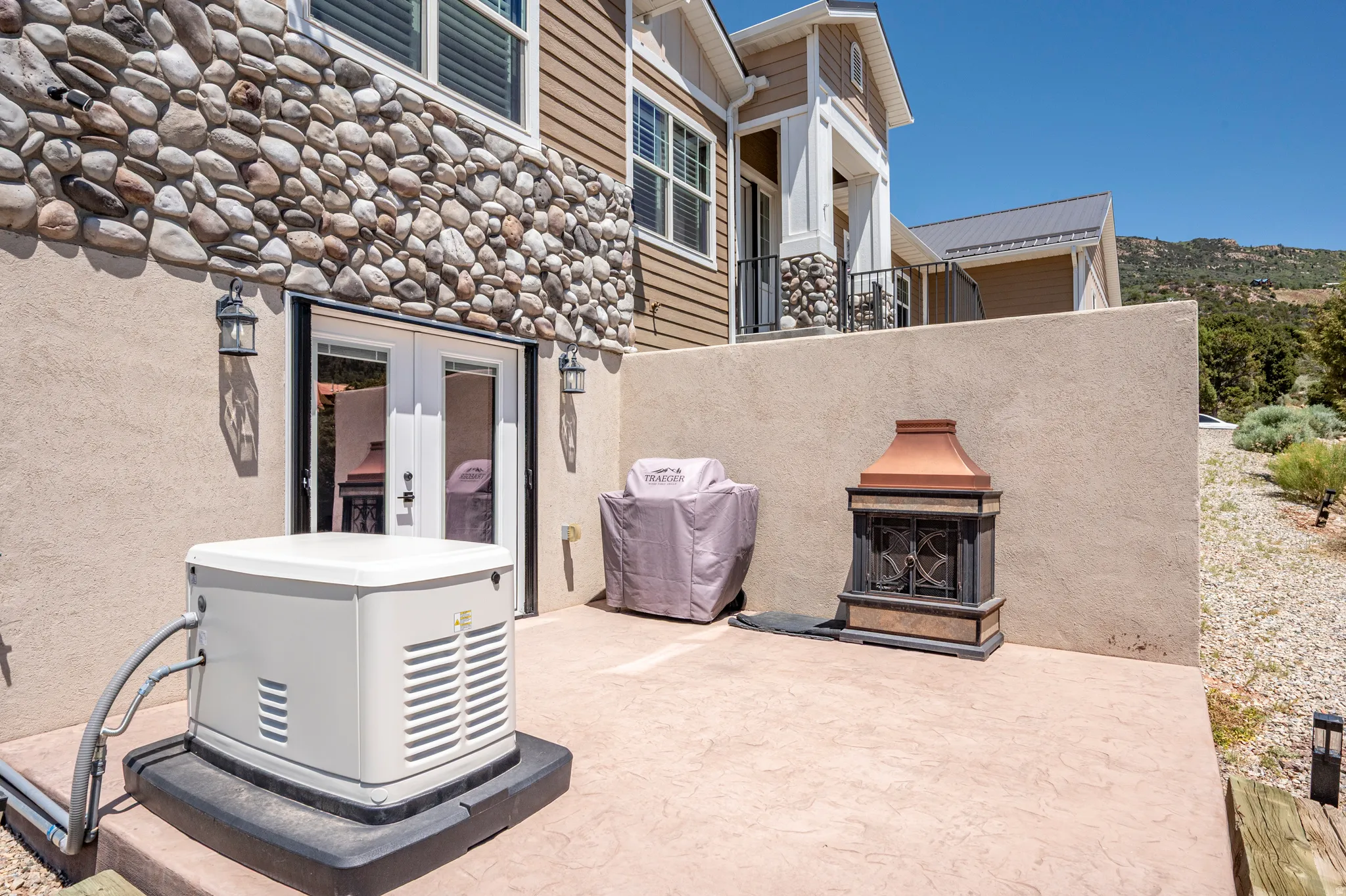 Stone veneer detailing, stucco exterior, double French doors, exterior wall lanterns, and a built-in outdoor fireplace