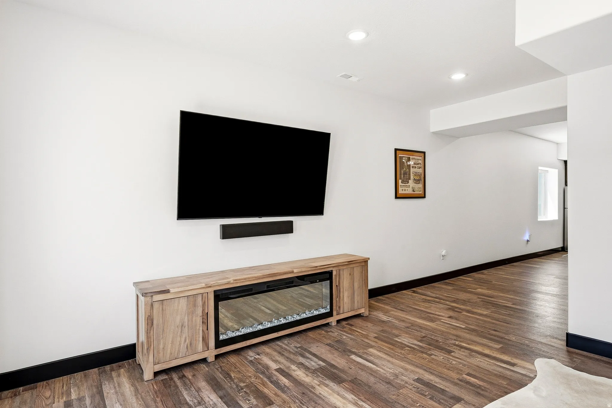 Wood-finish flooring, recessed lighting, and an electric fireplace insert within a wood-finish media console