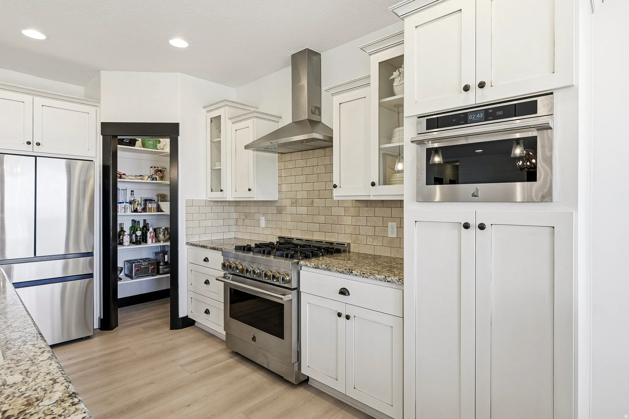 White cabinetry with dark hardware, stainless steel appliances, light wood-finish flooring, recessed lighting, and a walk-in pantry