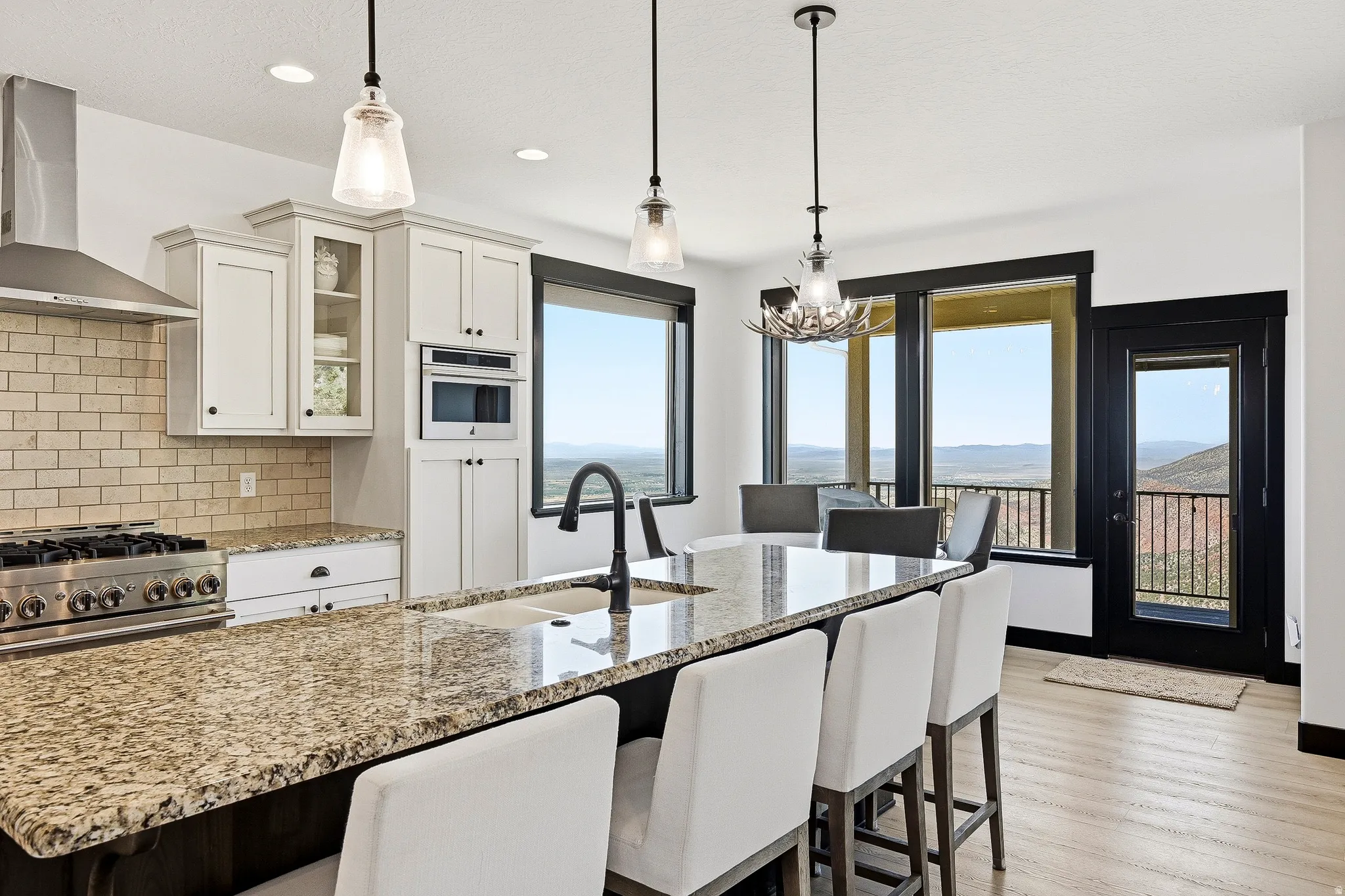 Kitchen featuring granite countertops, a built-in microwave, a stainless steel range hood, pendant lighting, and light wood-finish flooring
