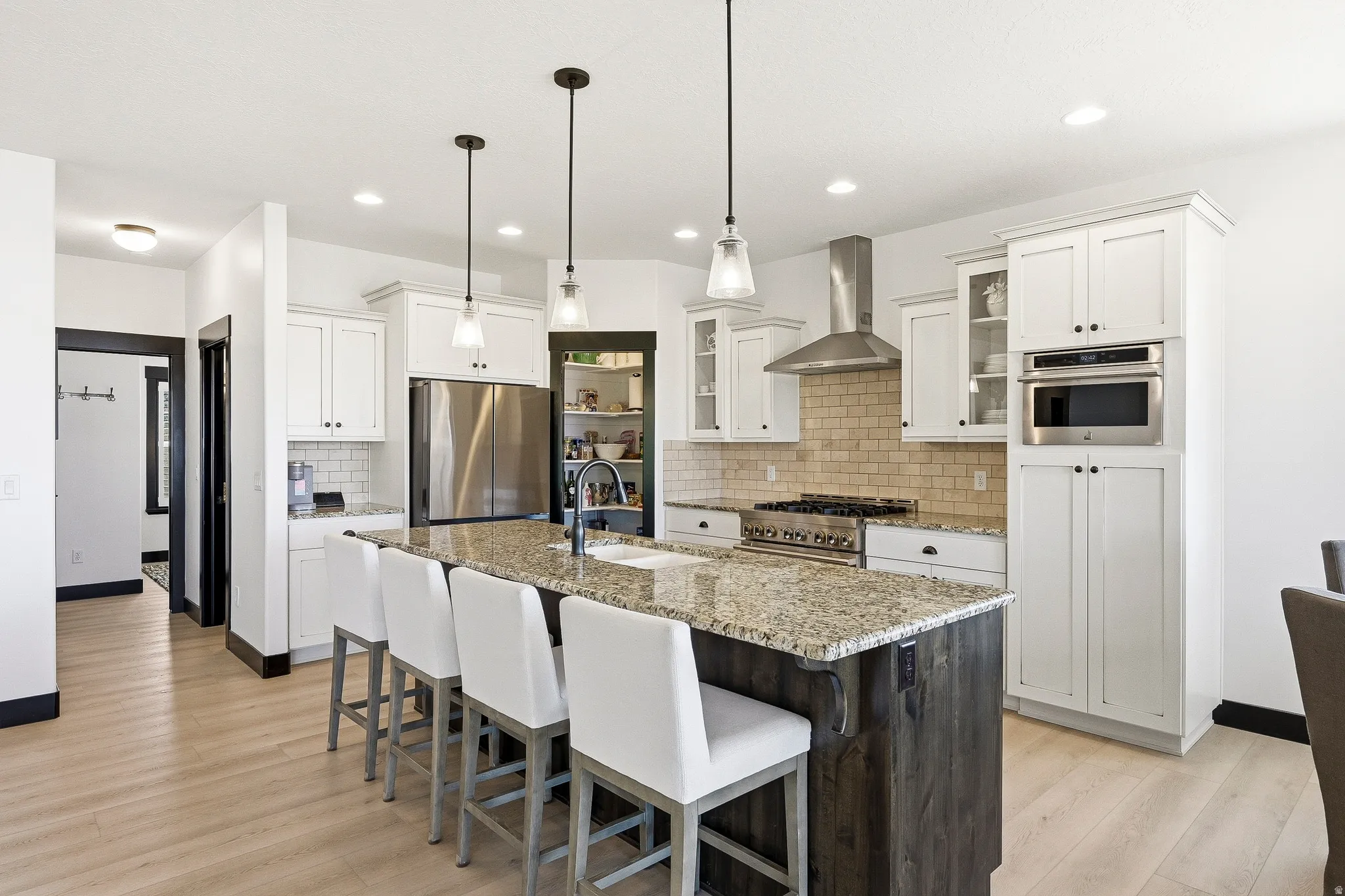 White cabinetry with black hardware, stainless steel appliances, light wood-finish flooring, and a central island with a stone-finish countertop
