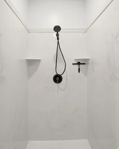 Shower enclosure with white swirled panels, dark bronze shower head and controls, and integrated corner shelves