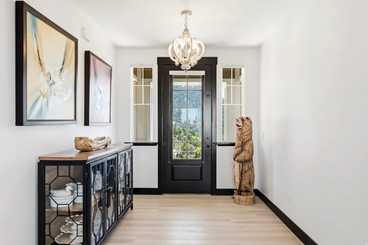Entryway featuring a dark-paneled door with frosted glass, side windows with grid patterns, a decorative chandelier, and wood-finish flooring