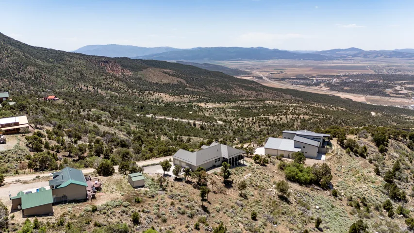 Expansive elevated property featuring a beige exterior, covered porch, and multi-pitched roofline, situated on a sloped hillside with distant mountainous terrain