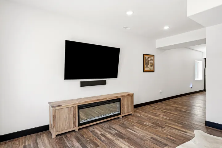 Wood-finish flooring, recessed lighting, and an electric fireplace insert within a wood-finish media console