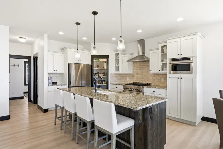 White cabinetry with black hardware, stainless steel appliances, light wood-finish flooring, and a central island with a stone-finish countertop