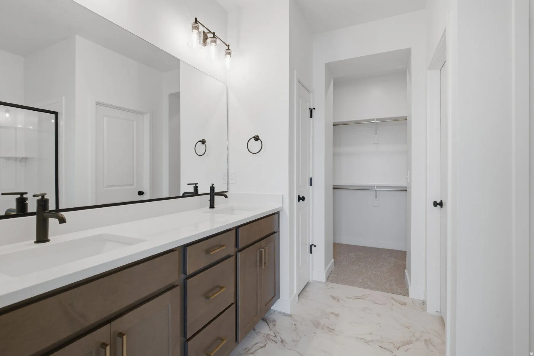 Dual vanity with integrated sinks, contemporary matte black fixtures, quartz countertops, wood-finish cabinetry, and a walk-in closet with shelving