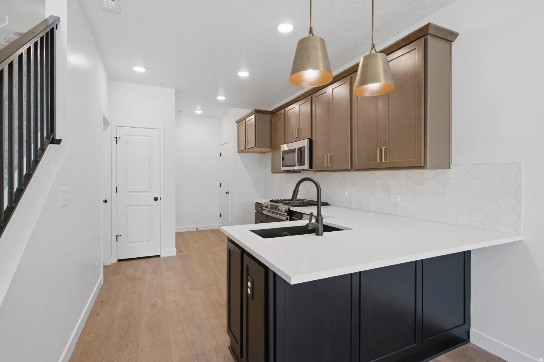 Kitchen featuring a black island with a white countertop, two pendant light fixtures, wood-finish flooring, and a stainless steel microwave