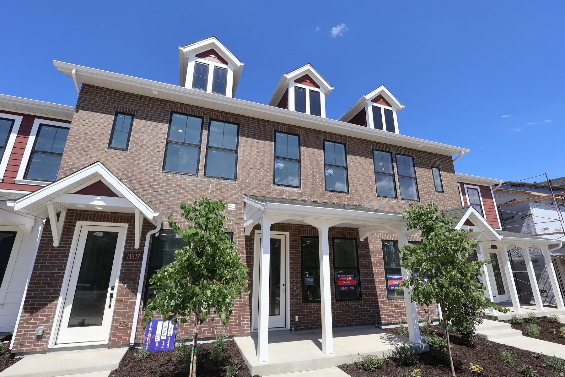 Brick and siding exterior with multiple dormer windows, covered front porch, concrete walkway, and newly planted landscaping