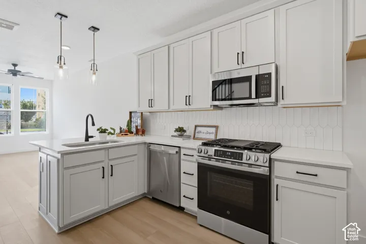 White shaker-style cabinetry with black hardware, stainless steel appliances, a white tile backsplash, a large kitchen island with an undermount sink, and wood-finish flooring