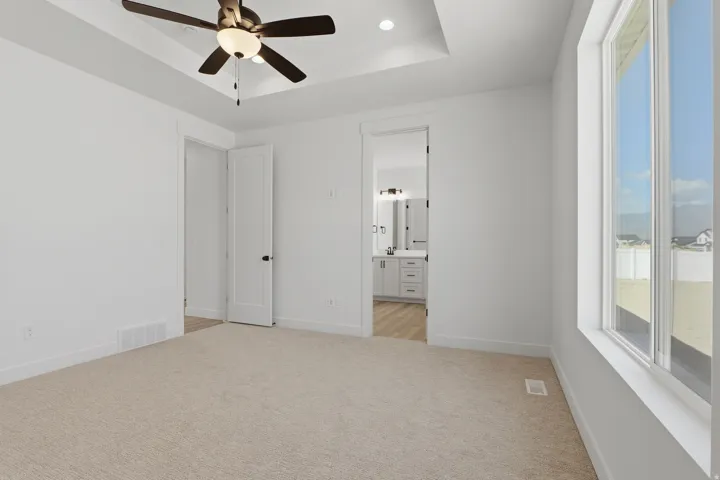 Tray ceiling with a ceiling fan, carpeted flooring, and white interior doors