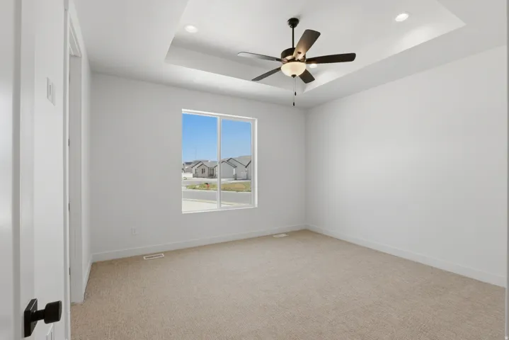 Recessed lighting, tray ceiling, ceiling fan, neutral carpeting, and a large window