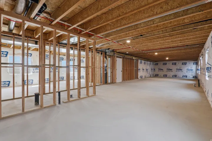 Unfinished basement with exposed wood framing, concrete flooring, and multiple window openings