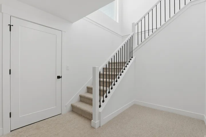 White interior door with black hardware, carpeted stairs with black metal balusters, and upper-level window