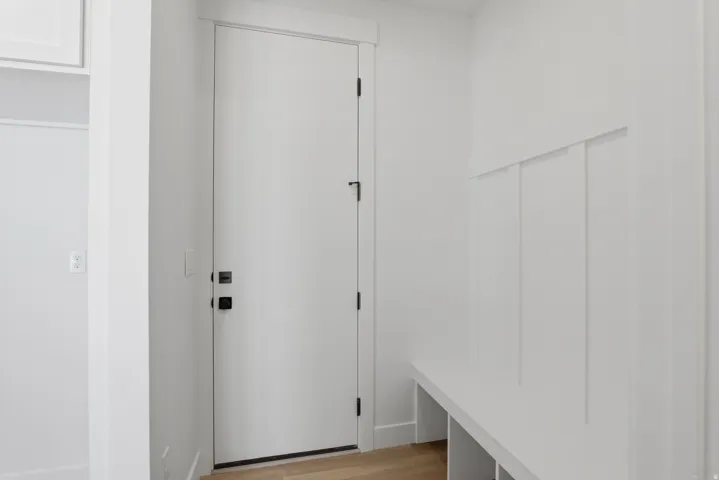 Entryway featuring a white door with matte black hardware, built-in bench seating, wood-finish flooring, and vertical paneling