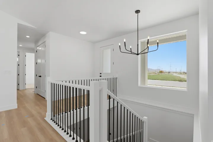 Upper landing with wood-finish flooring, white walls, recessed lighting, and a contemporary black chandelier