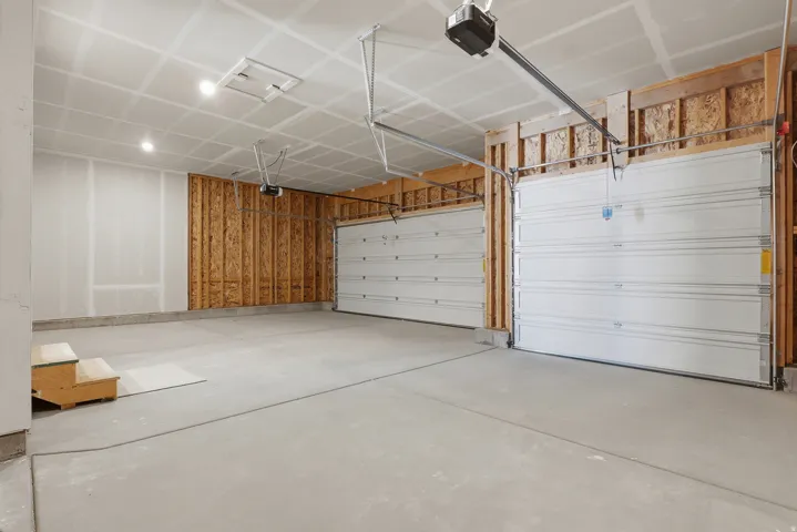 Spacious garage with exposed wood framing, two overhead garage doors, concrete flooring, and overhead lighting